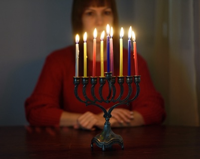 sad woman behind Hanukkah menorah, dealing with grief during the holidays. By Inna Reznik