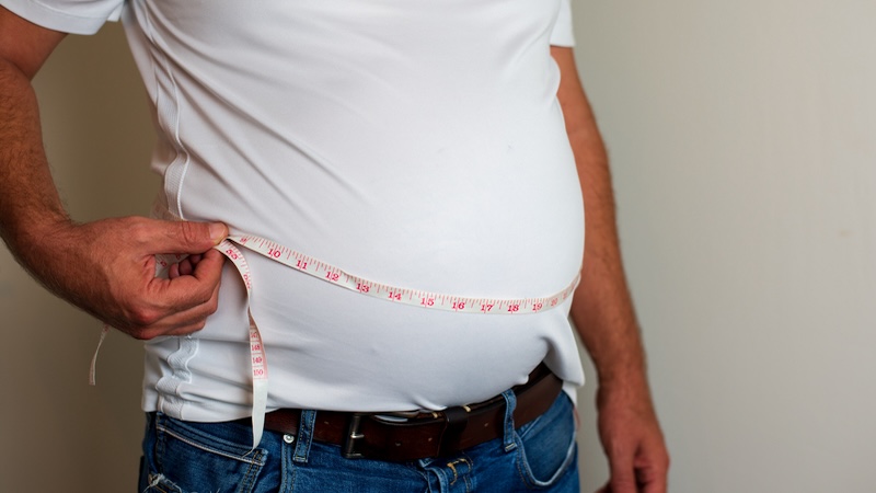 A man trying his best to measure his belly, illustrating how BMI is flawed.