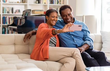 A couple sits on their home sofa taking a selfie. Even smartphones can be conduits for scams and fraud.