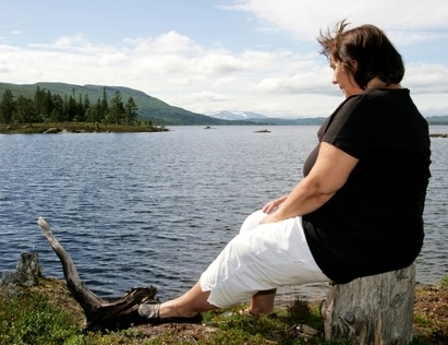 Woman sitting sad along lake.