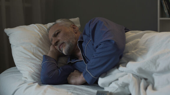 Man restless in bed suffering from poor sleep.