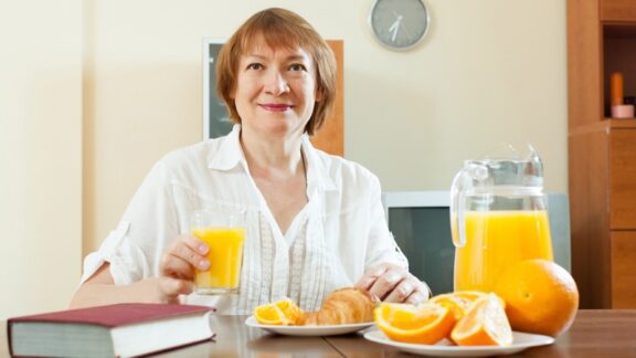 A woman eating breakfast with oranges and orange juice.