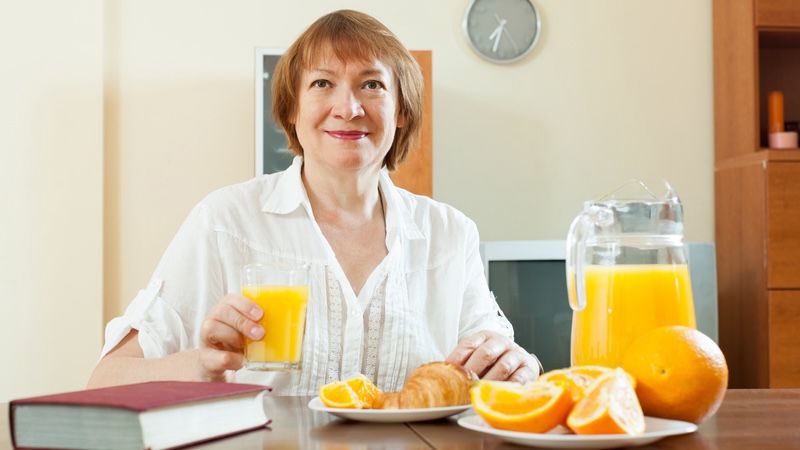 A woman eating breakfast with oranges and orange juice.