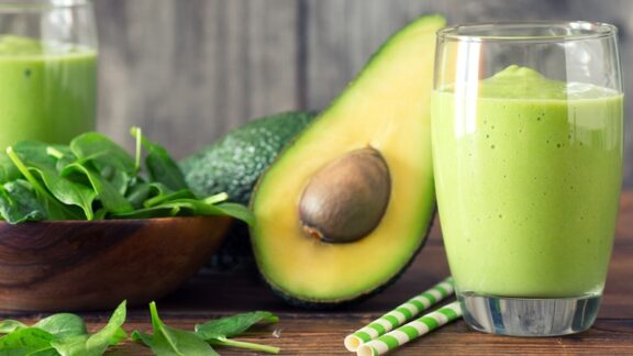 A healthy avocado sliced, along with a green smoothie next to it.