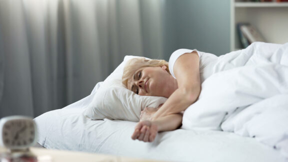 A contented woman in bed, having positive sleep habits. By motortion