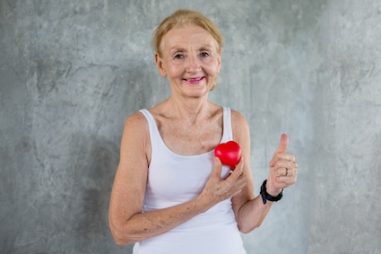 Woman with a toy heart, smiling and giving a thumbs up, having found support for healthy habits for her heart.