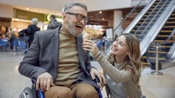 Man in a wheelchair with his granddaughter, enjoying an outing at a mall. Planning accessible outings can be key to enjoyment.