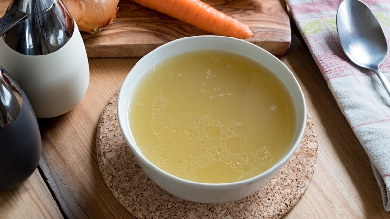 A bowl of bone broth with vegetables around it representing the benefits of bone broth