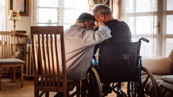 Sad couple at home with man in wheelchair, wondering if it's time to move to senior living. ND3000