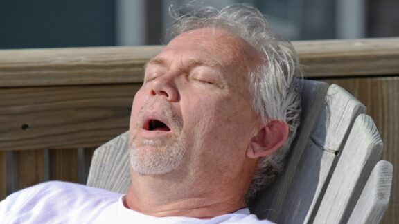 A man sleeping on a chair with his mouth open snoring.