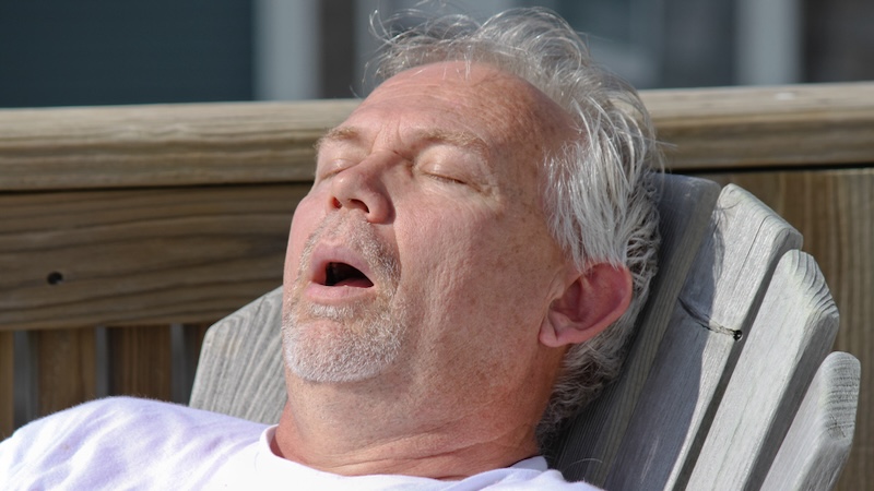 A man sleeping on a chair with his mouth open snoring.