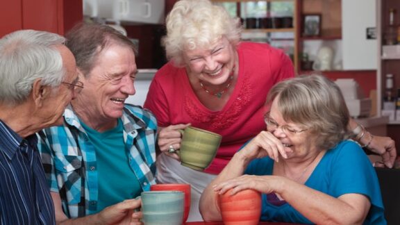 Four senior friends laughing together, feeling confident in public knowing how to feel comfortable with adult diapers. By Creatista