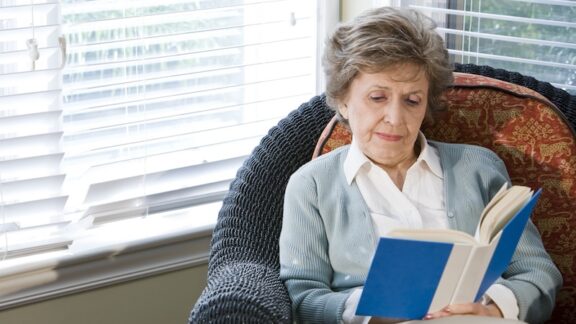 A middle-class senior woman reading at home. by Goldenkb. Mid-Income Seniors Face Housing Challenges