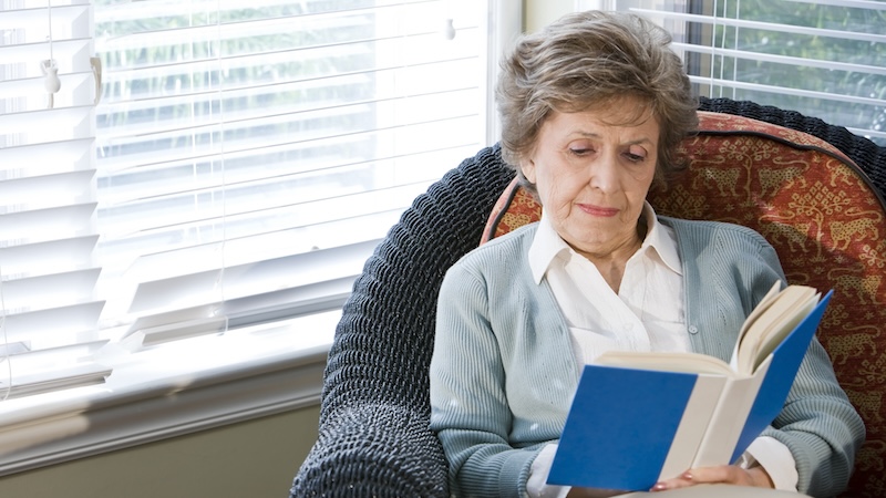 A middle-class senior woman reading at home. by Goldenkb. Mid-Income Seniors Face Housing Challenges