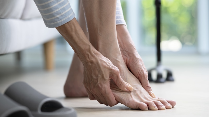 Knowing that foot care matters, a senior woman massages her feet. The base of a cane is visible in the background. Amenic181