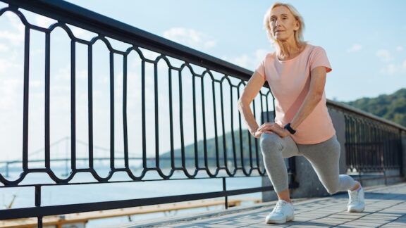 A senior woman during a workout outside, doing lunges for older adults
