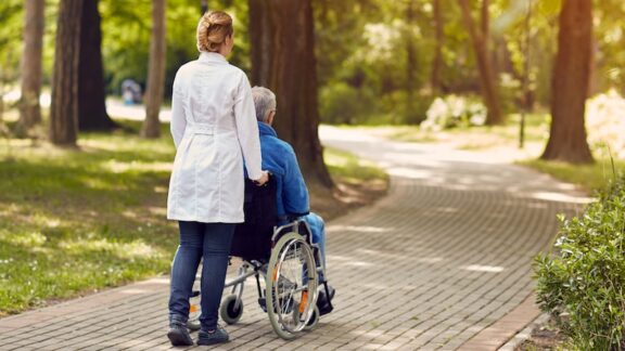 Planning for care is essential because of the likelihood of needing medical care in the future, like this senior being pushed down a sidewalk by a medical attendant. Image by Igor Mojzes.