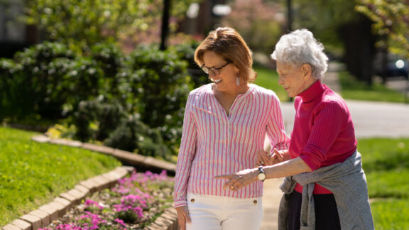 Naborforce Senior Lady Walking with Friend Pointing at Flowers