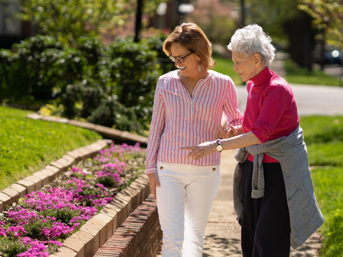 Naborforce Senior Lady Walking with Friend Pointing at Flowers