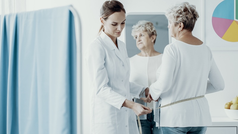 Woman at a doctor's office considering her weight. Patients need to know the facts behind the Medicare GLP-1 Bridge program while considering if the weight-loss drugs are right for them. Image by Bialasiewicz