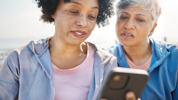 Two women looking in disbelief at a smartphone. You don’t know your phone's been hijacked till it loses service and you lose money. You’re the victim of SIM swapping, aka SIM hijacking. Yuri Arcurs