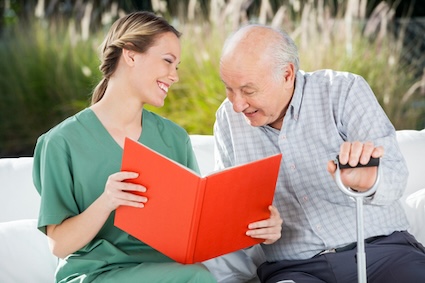 A nurse aide looks at a book with an elderly male patient. In choosing a memory care facility, ensure the staff is friendly and well-trained. Tyler Olson