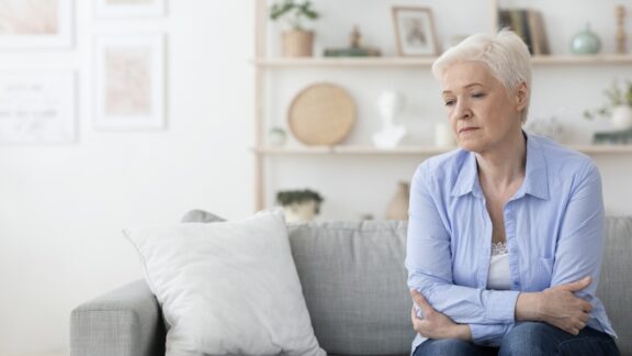 A solo ager worries about her future as she sits on a couch.