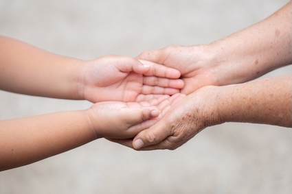 an adult's hands clasping a child's hands at intergenerational care centers. Aekkasit Rakrofjit