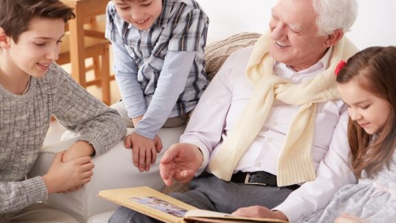 Every life is a story: granddad on a couch with three grandkids showing pictures