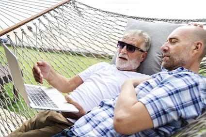 A gay couple on a hammock outside looking at a laptop. Rawpixelimages