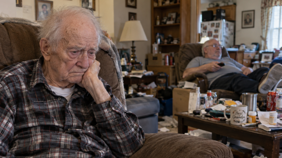 A sad abused elderly man and a messy house in the background, with the manipulative brother as caregiver