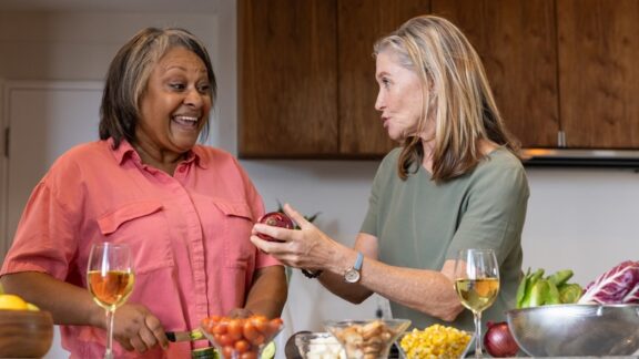 Two women who are using shared housing for seniors, cooking together in the kitchen. wavebreakmedia ltd