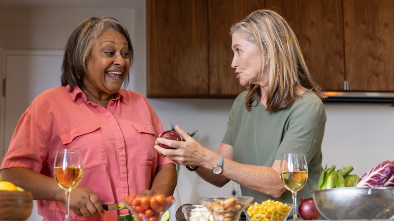 Two women who are using shared housing for seniors, cooking together in the kitchen. wavebreakmedia ltd