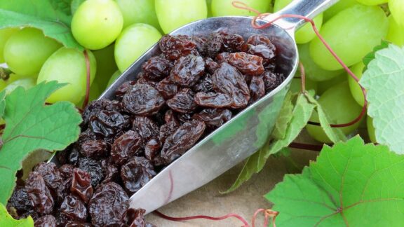 A scoop of healthy raisins with white grapes behind it.