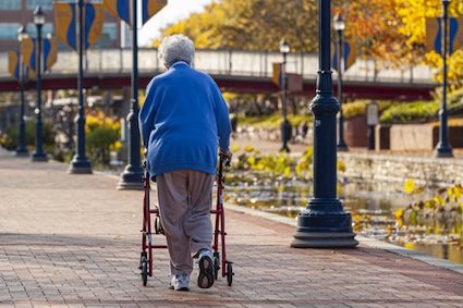 Woman walking along a sidewalk using her rollator, aware of walking safety tips. Credit Grandbrothers